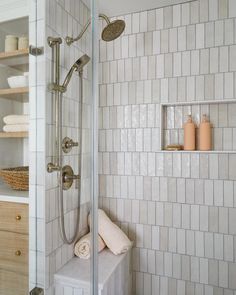 a white tiled bathroom with shelves and towels on the shower wall, along with an open shelving unit