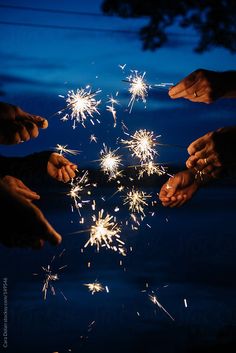 several people holding sparklers in their hands at night with blue sky and clouds behind them