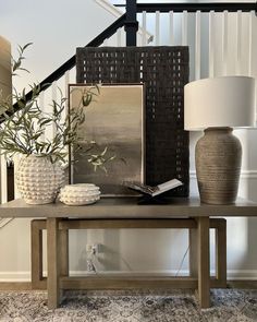 a wooden table topped with vases next to a lamp and painting on the wall