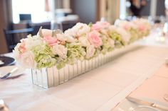 a table with white and pink flowers in vases on top of each other, along with silverware