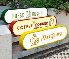 two coffee signs sitting on the side of a cement wall next to flowers and potted plants