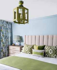 a bedroom with blue walls, green and white bedding and a light fixture hanging from the ceiling