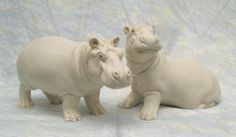 two white ceramic hippos sitting next to each other on a blue and white background