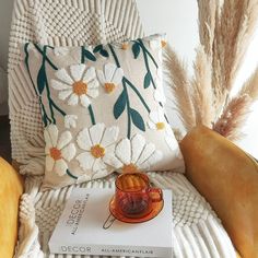 a book sitting on top of a white chair next to a pillow and some flowers