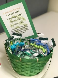 a green basket filled with assorted items sitting on top of a table next to a sign