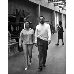 black and white photograph of man and woman walking down the street in an industrial area