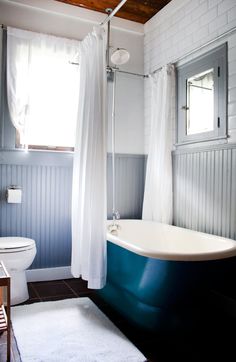 a bath tub sitting next to a white toilet in a bathroom under a wooden ceiling