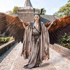 a woman dressed as a demon with wings on her head and arms outstretched in front of a castle