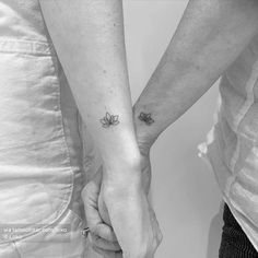 two people holding hands with small tattoos on their arms and one is holding the other's hand