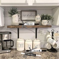 coffee mugs are lined up on a shelf above the kitchen counter, along with cups and saucers