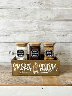 three jars of spices sitting on top of a wooden box with the words mores station