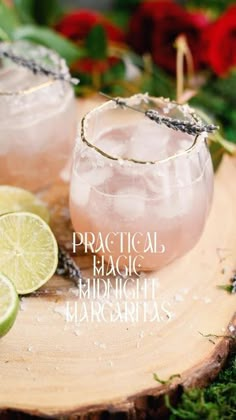 two margaritas sitting on top of a wooden table next to lime slices and flowers