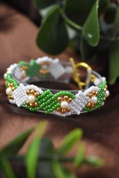 a green and white beaded bracelet sitting on top of a wooden table next to a plant