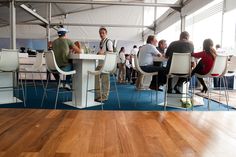 people are sitting at tables in a large room with wooden floors and white walls, while one man is talking on the phone