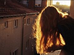 a woman standing on top of a roof looking out at the sun shining through her window