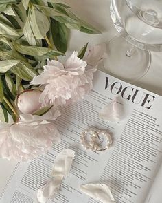 an open book with flowers and pearls on it next to a glass of wine,