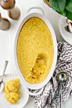 a white casserole dish filled with cornbread next to two plates and spoons