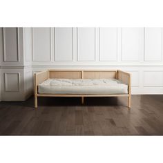 a wooden day bed sitting on top of a hard wood floor next to a white wall