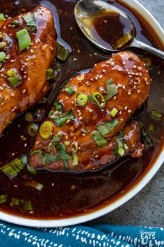 two pieces of chicken covered in sauce and green onions with sesame seeds on the side