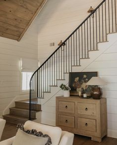 a living room with white walls and wooden floors next to a stair case in front of a window