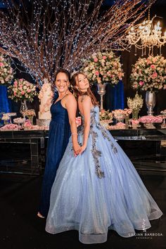 two girls in blue dresses standing next to each other at a formal event with chandeliers and flowers