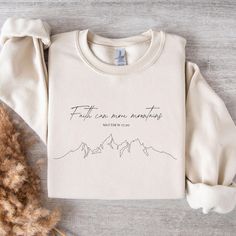 a white sweatshirt with the words faith has never meant written on it and mountains in the background