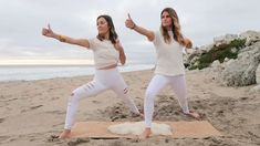 two women doing yoga on the beach with their arms in the air and thumbs up