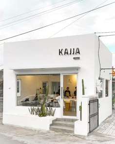 a small white building with people sitting at tables in it's front window and the words kaua written on the door