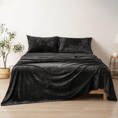 a bed with black sheets and pillows on top of it next to a potted plant