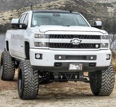 a white truck parked on top of a dirt field next to a lake and mountains