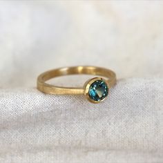 Gold engagement ring lays flat and to an angle so you can see the side of the ring. There is a bi-colour green/blue gemstone in the centre of the ring held in place with a dainty metal halo. Yellow Gold Sapphire Ring, Mint Green, Turquoise Ring, Sapphire Ring, Handcrafted Jewelry