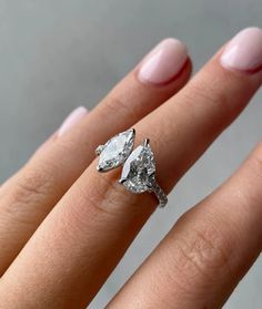 a woman's hand wearing a ring with two pear shaped diamonds on the side