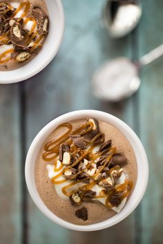 two white bowls filled with chocolate and caramel toppings on top of a wooden table