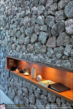 a stone wall with books and vases on the shelf next to it, along with other items