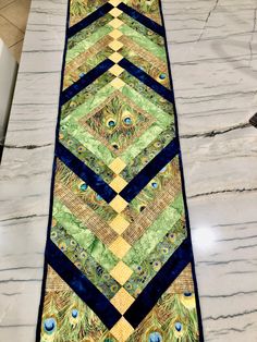 a quilted table runner with peacocks and feathers on the border, sitting on a marble countertop