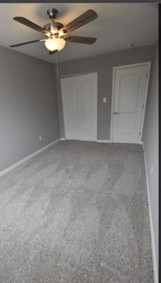 an empty room with carpet and ceiling fan in the corner, two doors are open