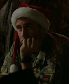 a man wearing a santa hat sitting in front of a christmas tree with his hand on his chin