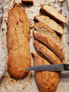 a loaf of bread, sliced and sitting on top of parchment paper with a knife next to it