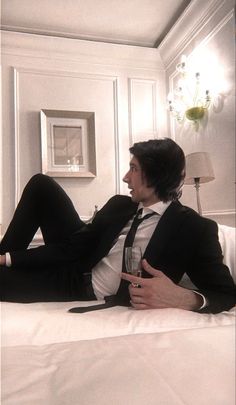 a man in a suit and tie laying on a bed with his legs crossed, looking off to the side