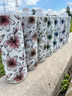 four different colored cups sitting on top of a cement wall next to grass and trees