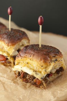 two mini sandwiches with meat and cheese on them sitting on top of brown wax paper