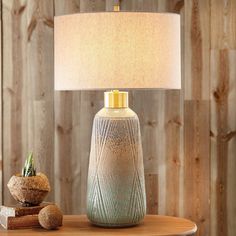 a table with a lamp on it and some rocks sitting next to it in front of a wooden wall