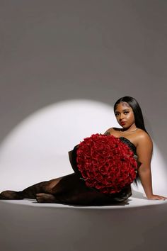 a woman sitting on the ground holding a large red flower