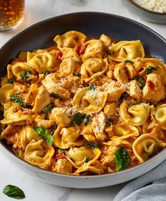 pasta with chicken and spinach in a bowl next to a glass of beer on the side