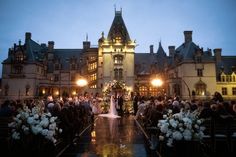 a bride and groom are standing in front of a large building with flowers on the aisle