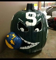 a green and white pumpkin with a face painted on it's side next to a blue ball