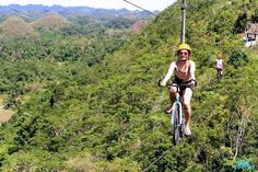 a man riding a bike down a zip line in the jungle with other people watching