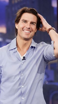 a smiling man in a blue shirt is holding his hand to his head and looking at the camera