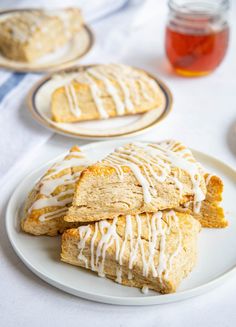 three scones with white icing sitting on a plate next to some honey jars