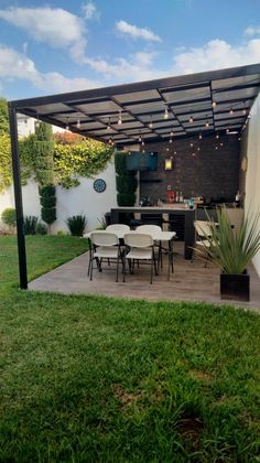 an outdoor patio with table and chairs under a pergolated roof, surrounded by green grass